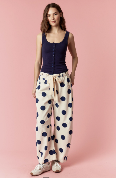 Woman wearing a navy tank top and polka dot pants on a pink background