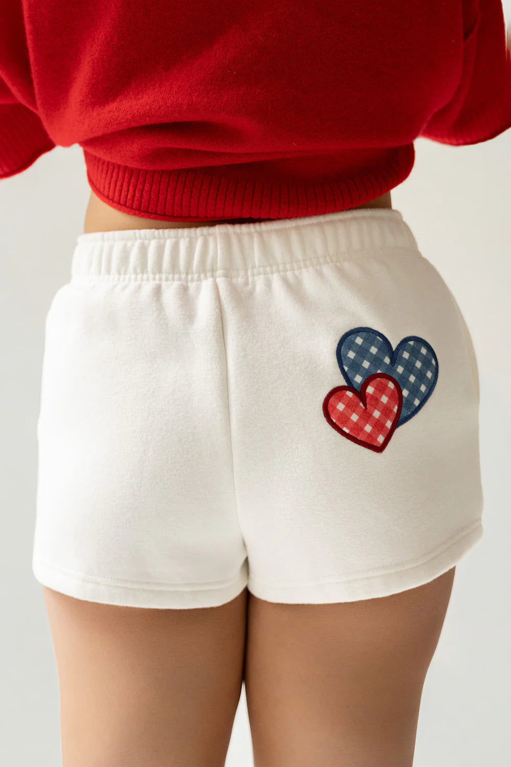 White shorts with a heart design worn by a person in a red top on a light gray background