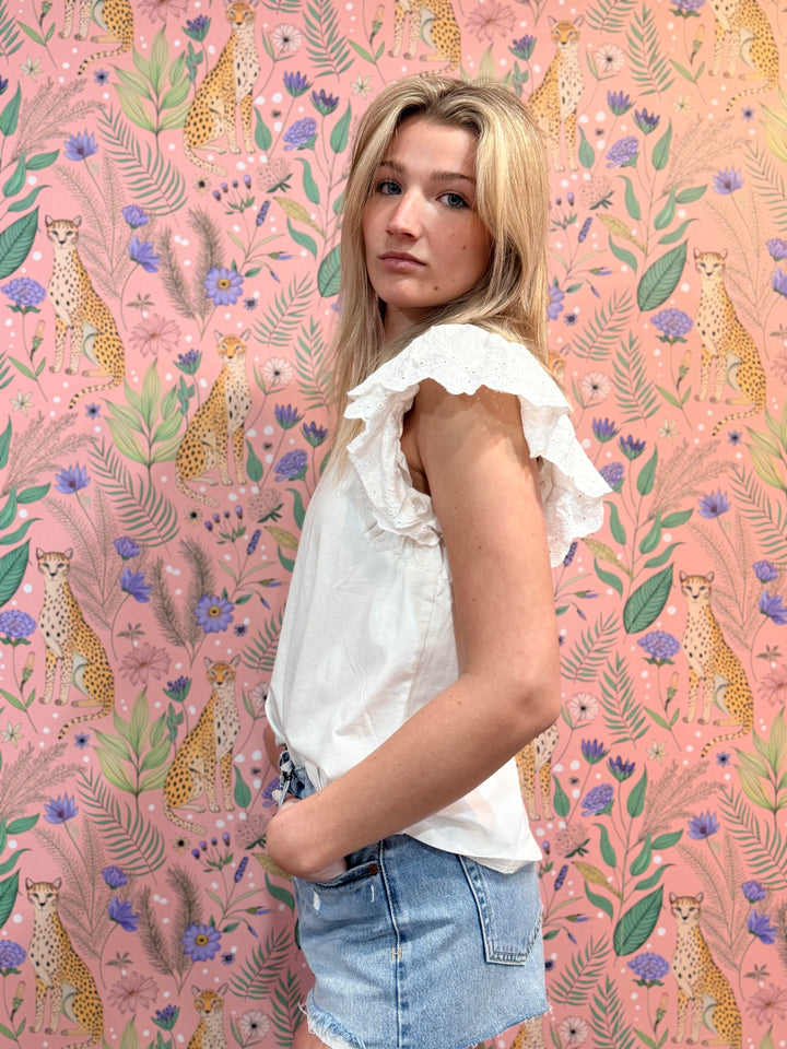 Woman wearing a white blouse and denim shorts against a pink background with animal and floral patterns.