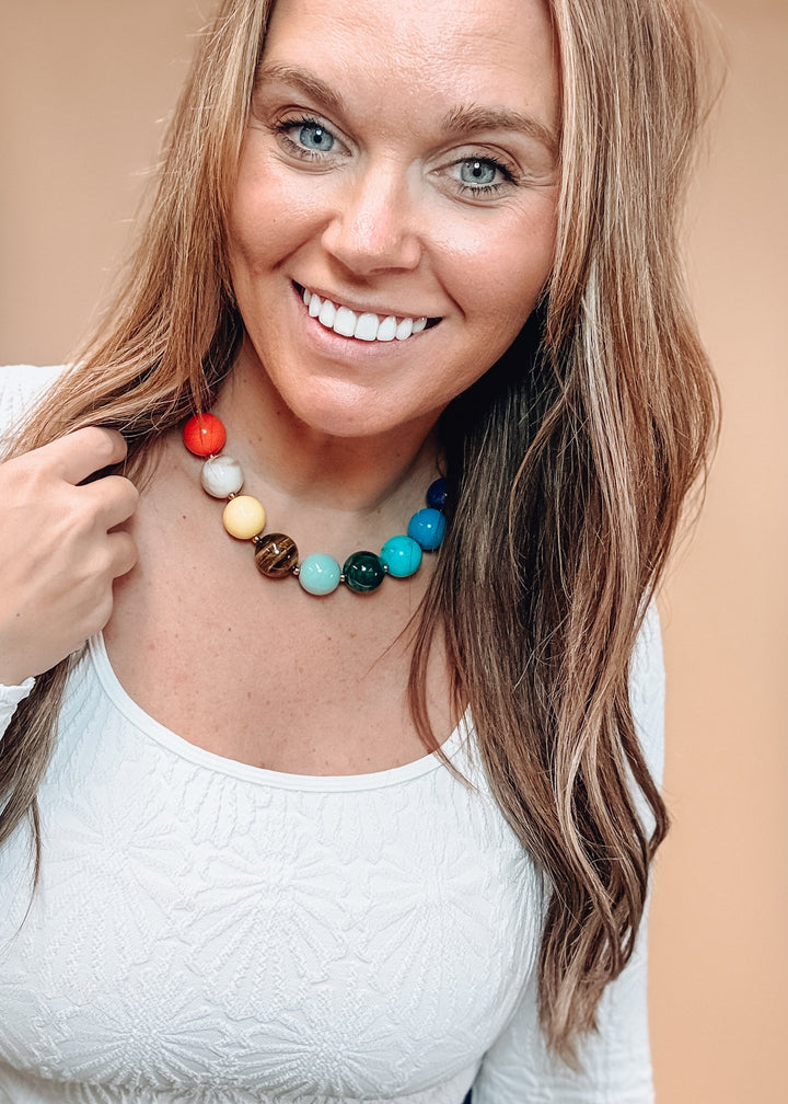 Woman wearing white top and colorful beaded necklace on plain background