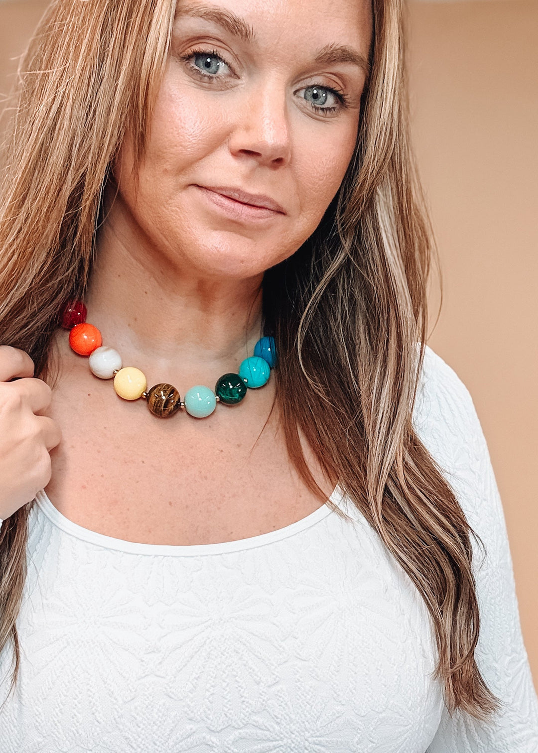 Woman wearing white shirt and colorful beaded necklace on plain background