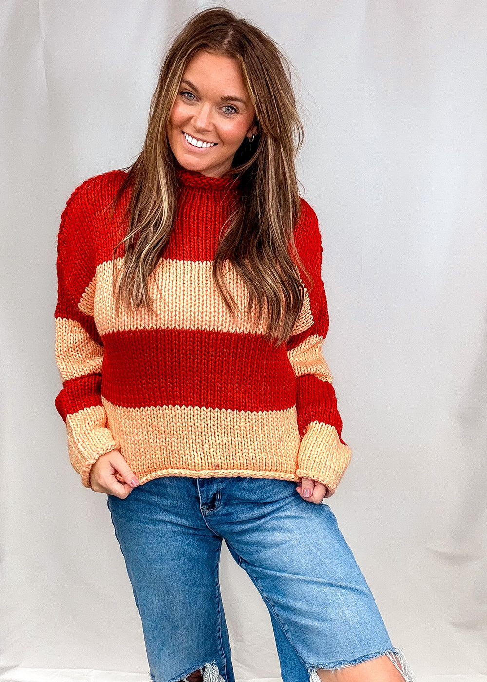 Woman wearing red and orange stripe sweater with jeans on plain background