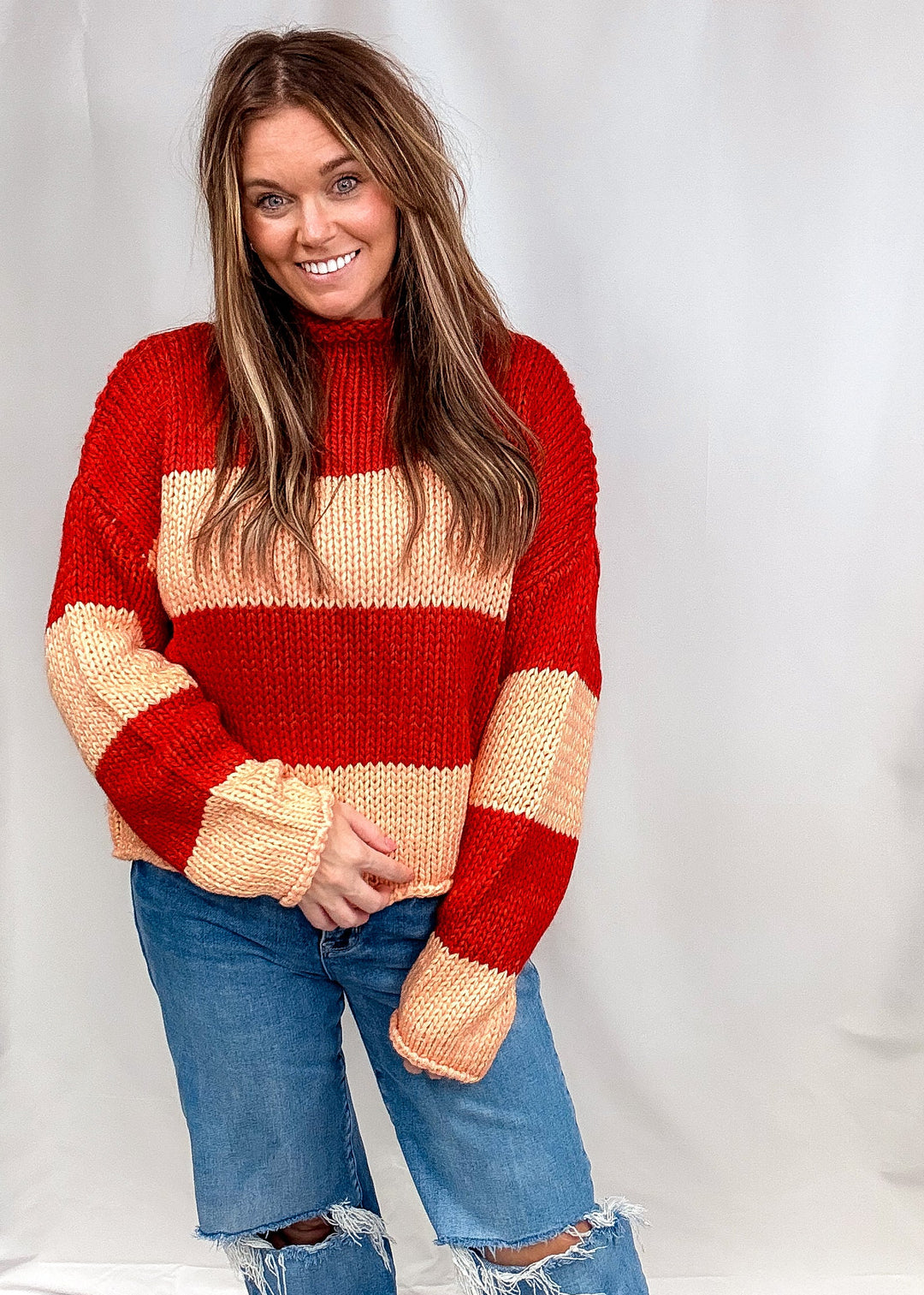 Woman wearing red and orange stripe sweater and jeans on plain background