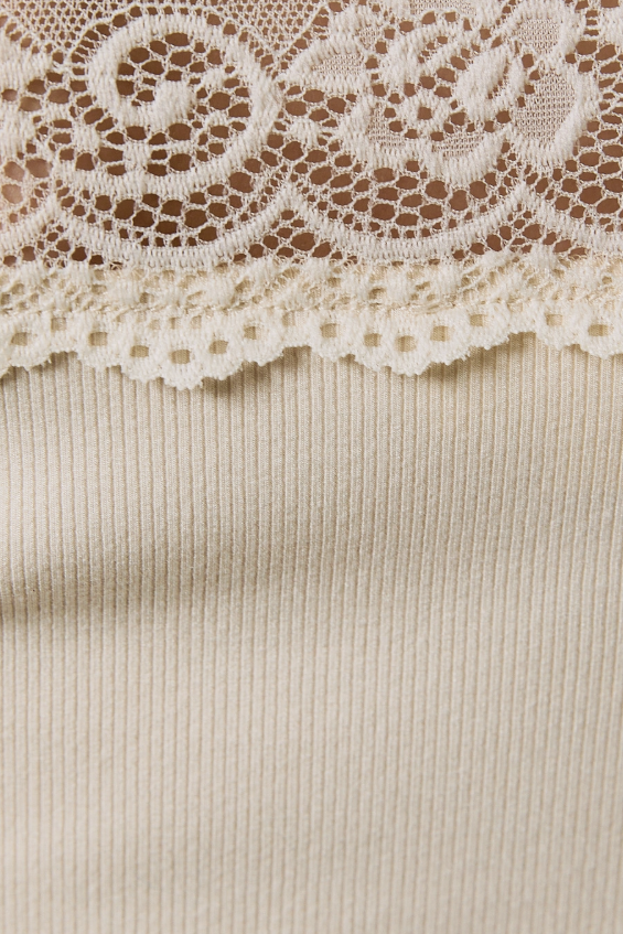 Close-up detail of a cream-colored ribbed knit garment featuring a decorative floral lace trim across the upper portion.