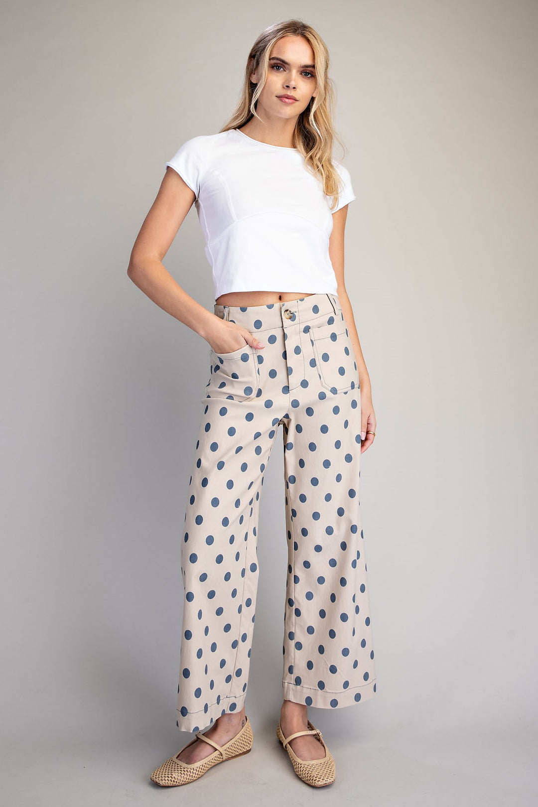 Woman wearing a white crop top and patterned pants on a gray background
