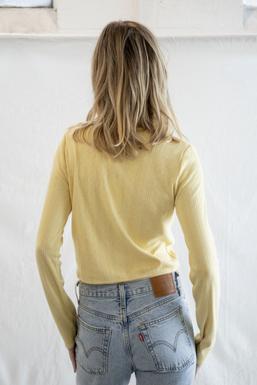 Woman shown from behind wearing yellow cardigan and jeans on plain background