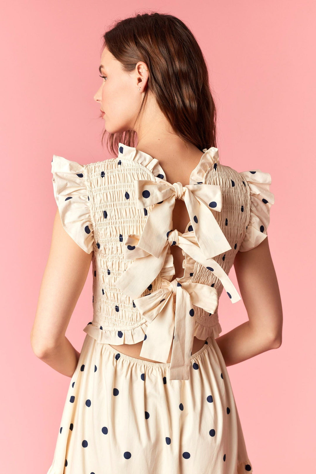 Woman wearing a polka dot dress with ruffled sleeves and bows on a pink background