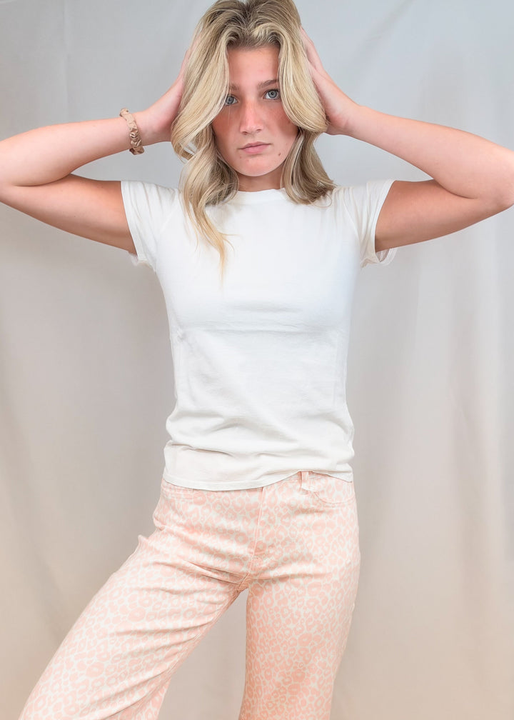 Woman wearing white baby tee with pink leopard pants on plain background