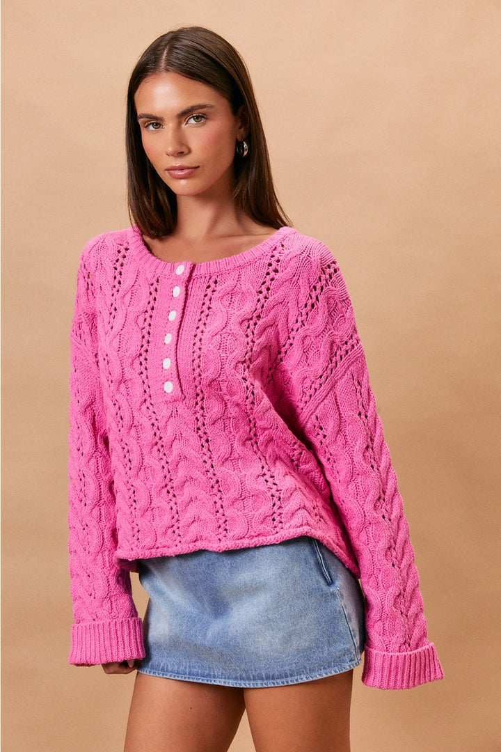 Woman wearing pink cable knit sweater and denim skirt on plain background