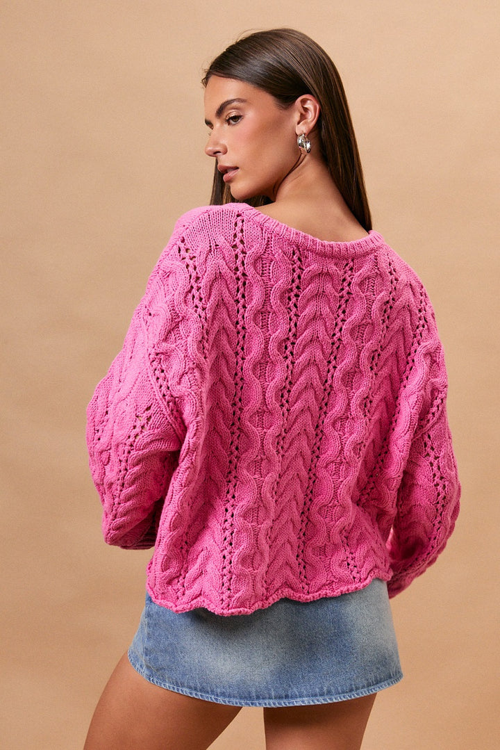 Woman wearing pink cable knit sweater and denim skirt on plain background