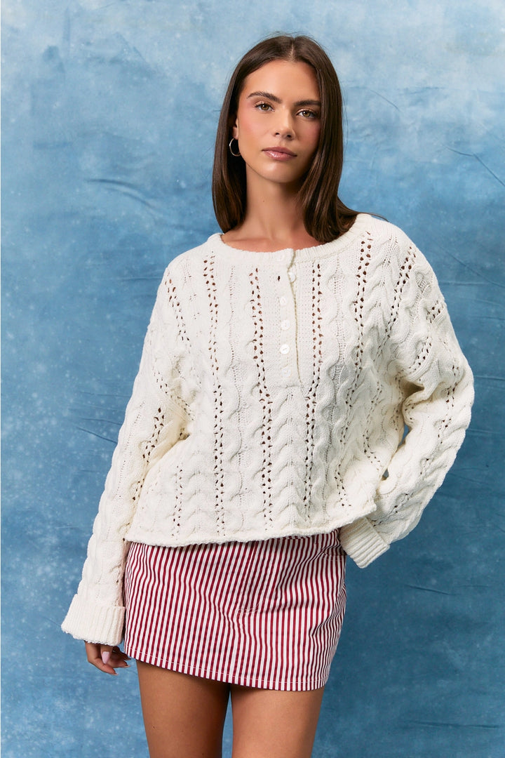 Woman wearing white cable knit sweater and skirt on blue background