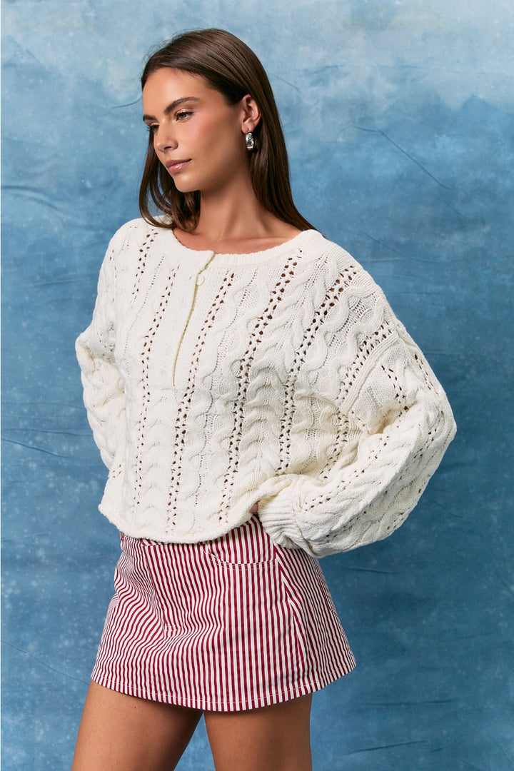 Woman wearing white cable knit sweater and skirt on blue background