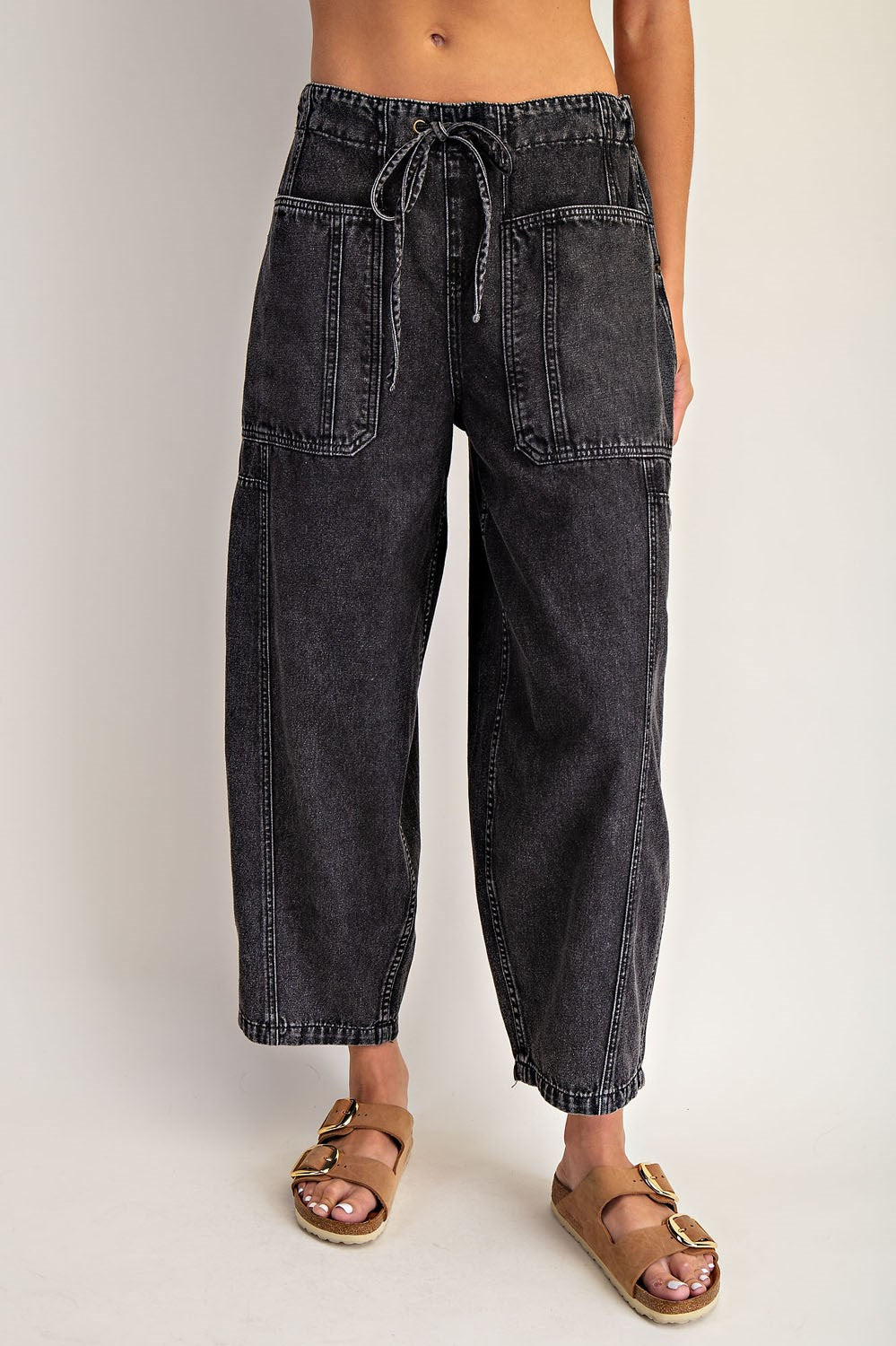 Person wearing black denim pants with a tie waist on a plain background