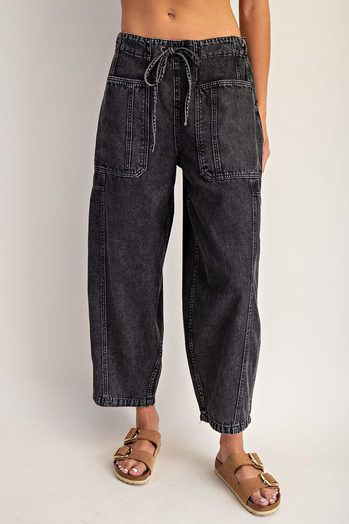 Person wearing black denim pants with a tie waist on a plain background