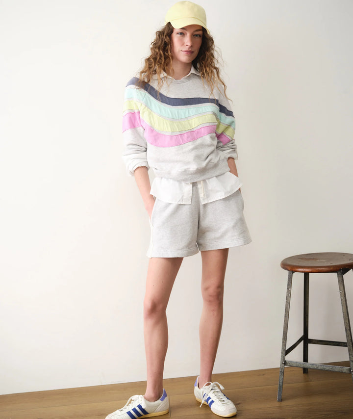Person wearing a colorful striped sweater and gray shorts with a yellow cap indoors.