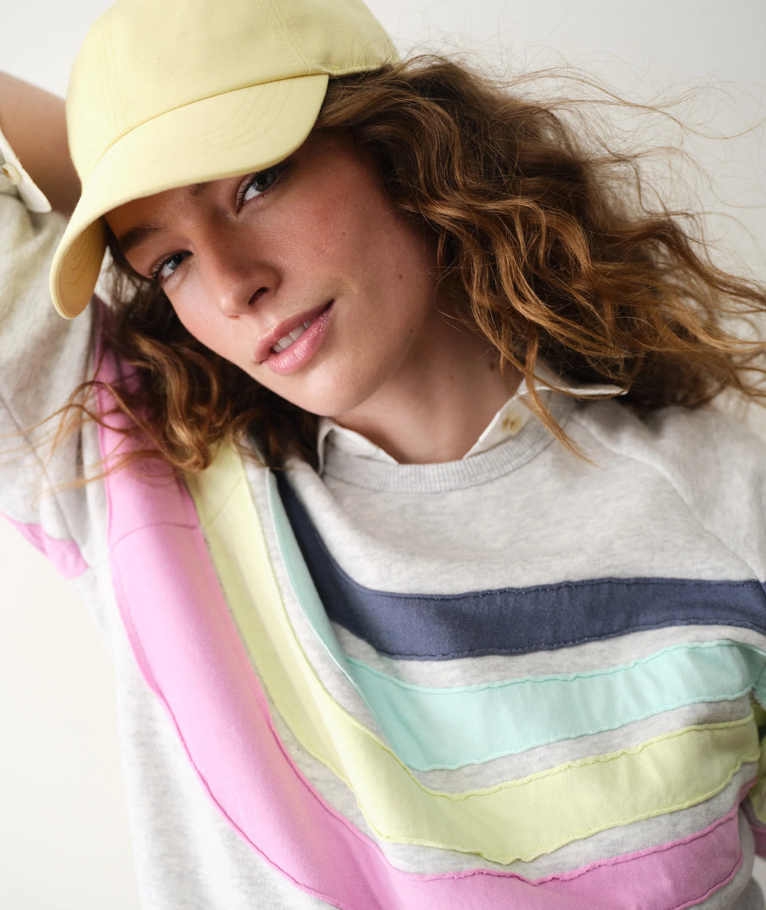Woman wearing a yellow cap and colorful striped sweater on a white background