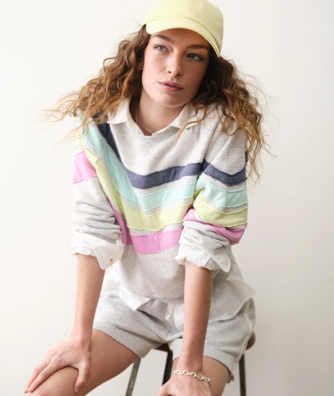 Person wearing a colorful striped sweater and light-colored shorts with a yellow cap.