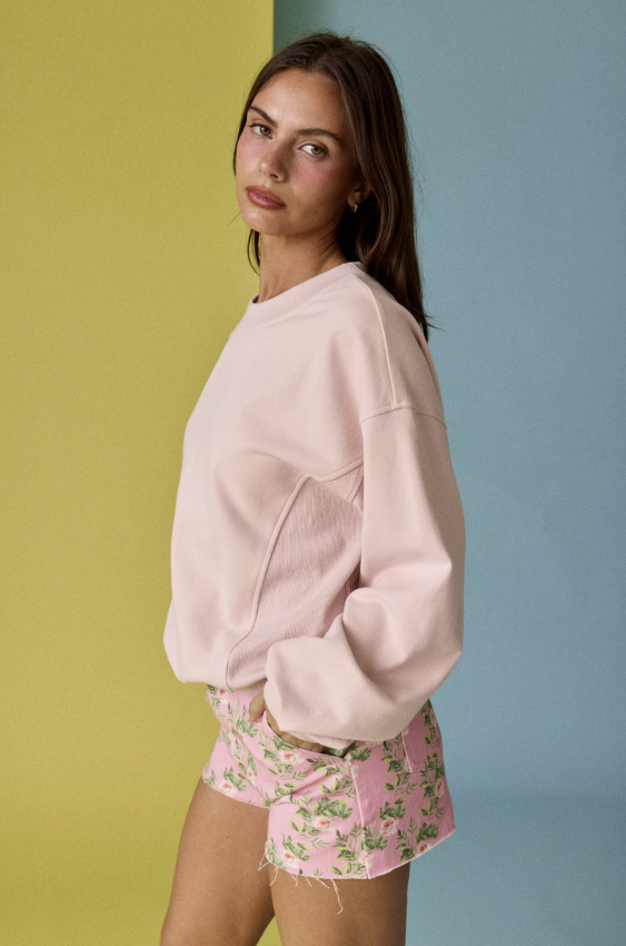 Woman wearing a pink sweatshirt and floral shorts against a multicolored background