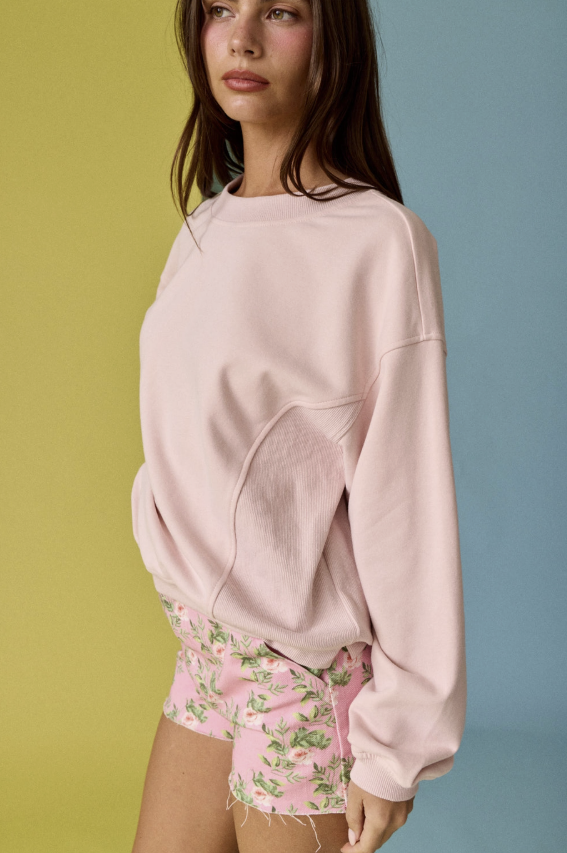 Woman wearing a pink sweatshirt and floral shorts against a multicolored background