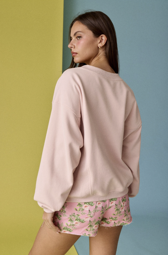 Woman wearing a light pink sweatshirt and floral shorts against a multicolored background