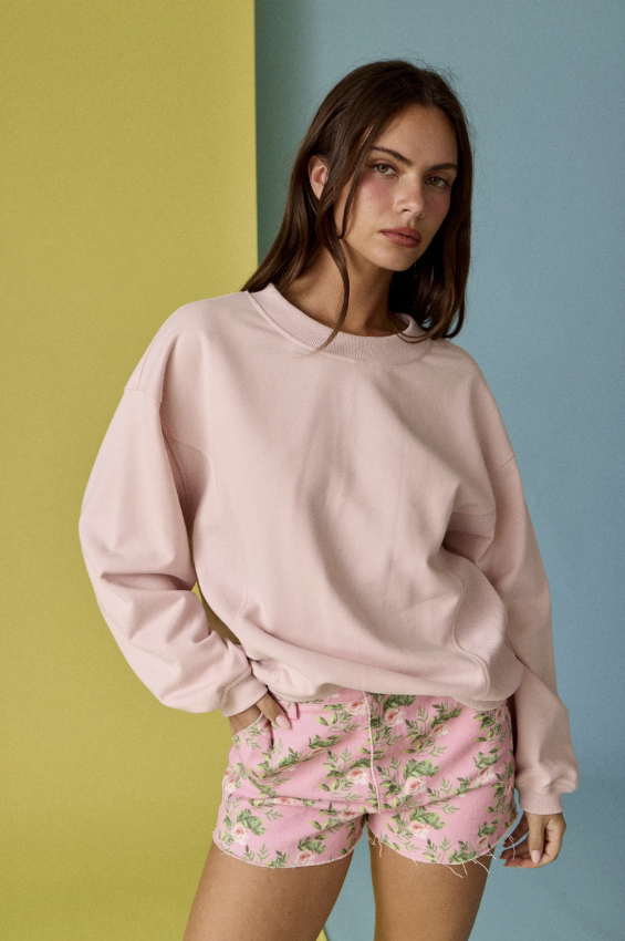 Woman wearing a pink sweatshirt and floral shorts against a colorful background