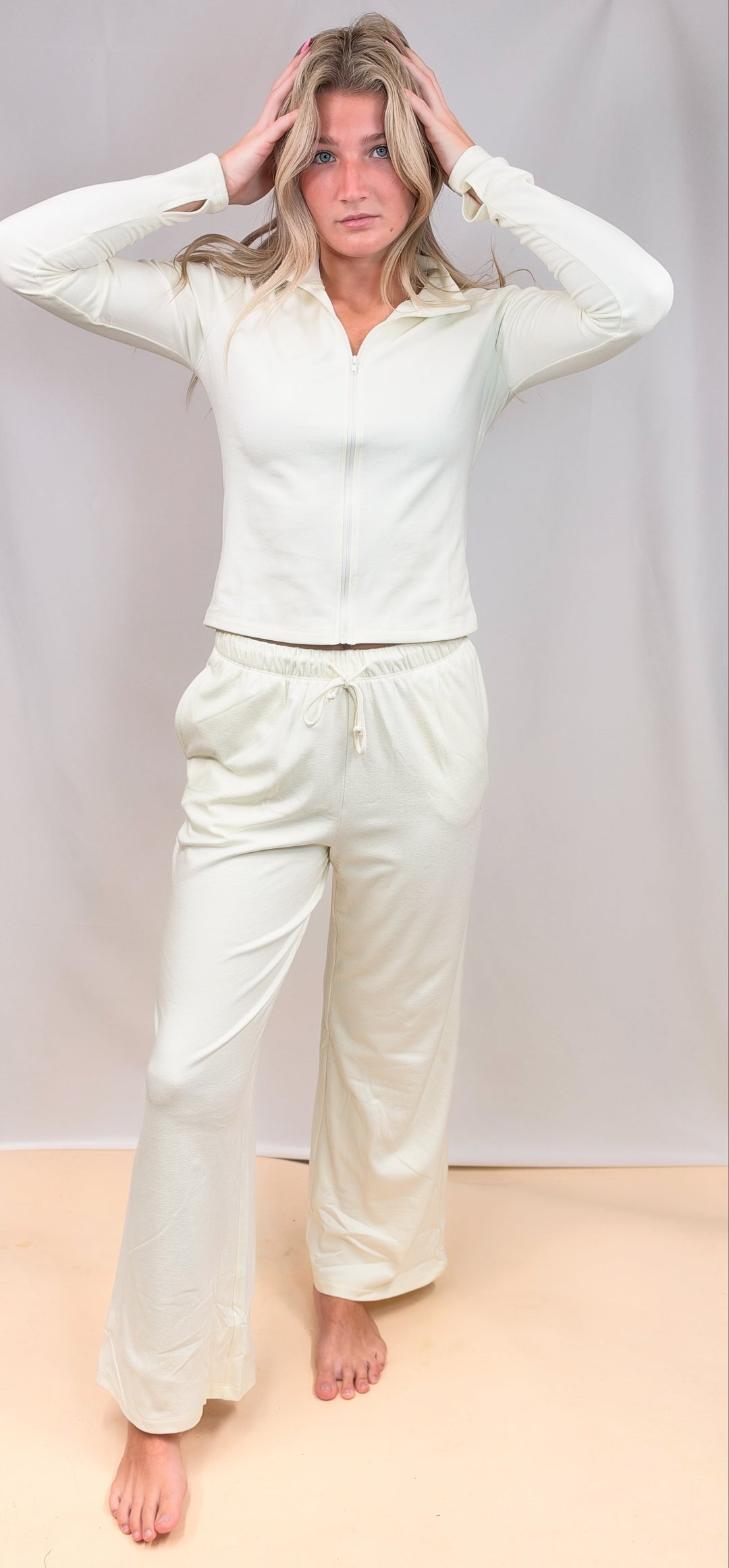 Woman wearing cream matching set with zip up top and pants on plain background