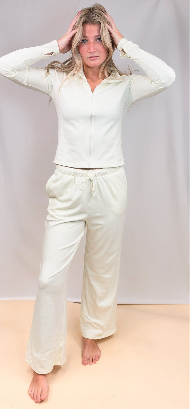Woman wearing cream matching set with zip up top and pants on plain background