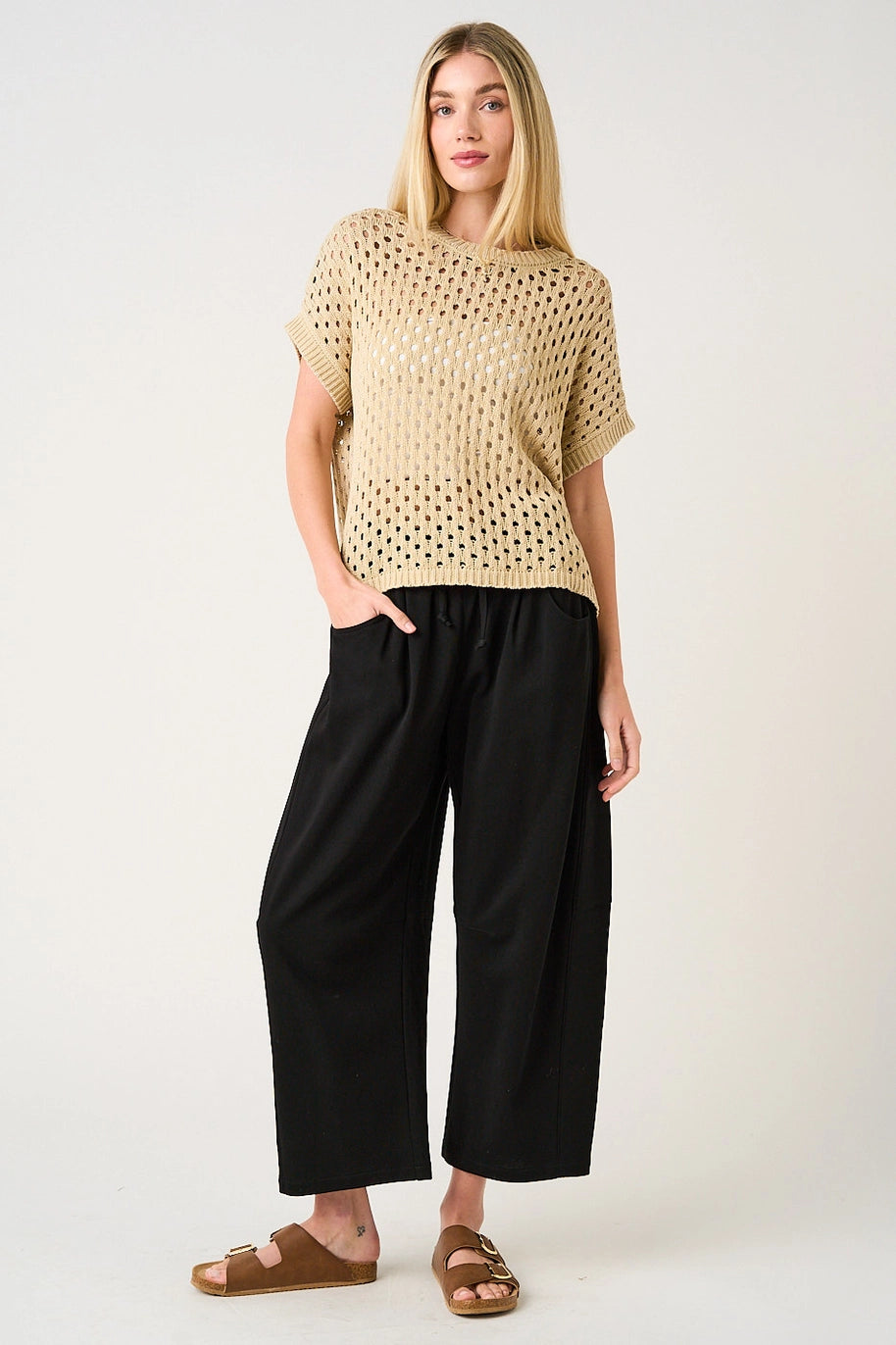 Woman wearing a beige knitted top and black wide-leg pants on a white background