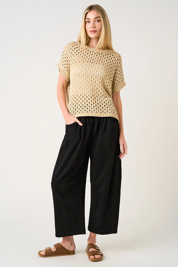 Woman wearing a beige knitted top and black wide-leg pants on a white background