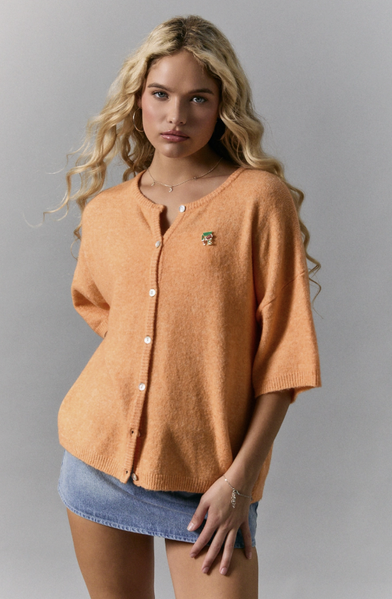 Woman wearing an orange button-up shirt and denim skirt against a gray background