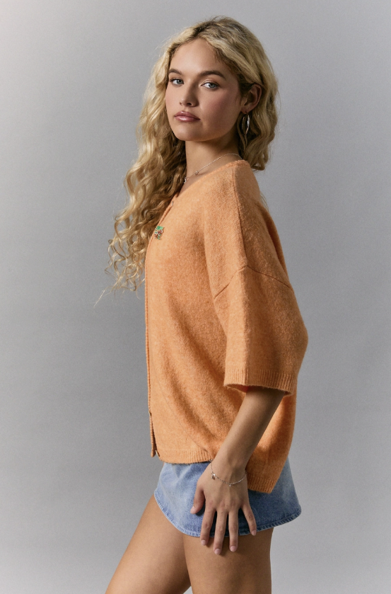 Woman wearing a peach-colored sweater and denim shorts against a gray background