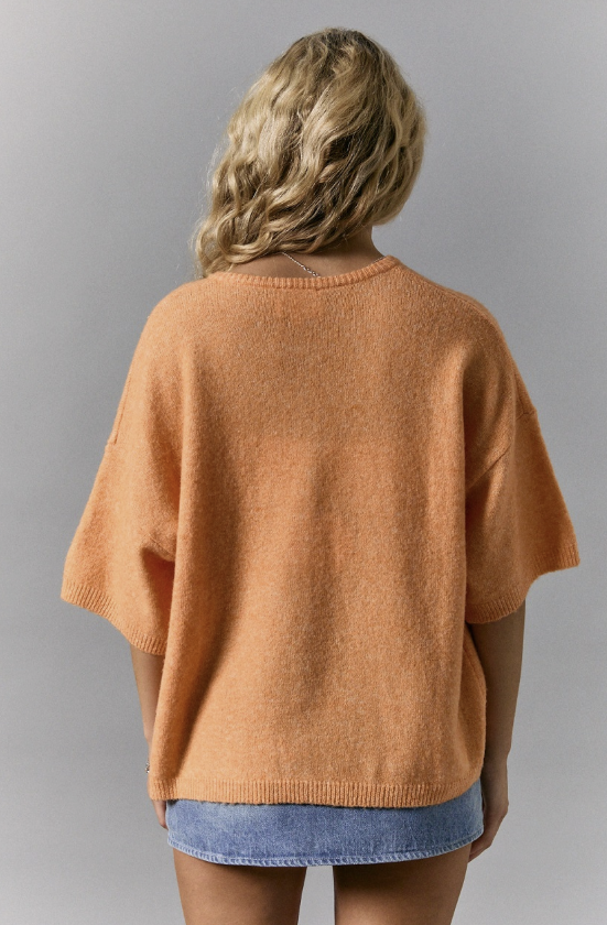 Person wearing a brown sweater and denim shorts on a gray background