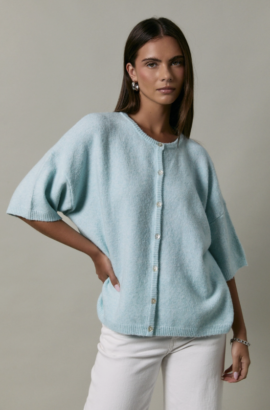 Woman wearing a light blue knitted sweater with short sleeves against a neutral background
