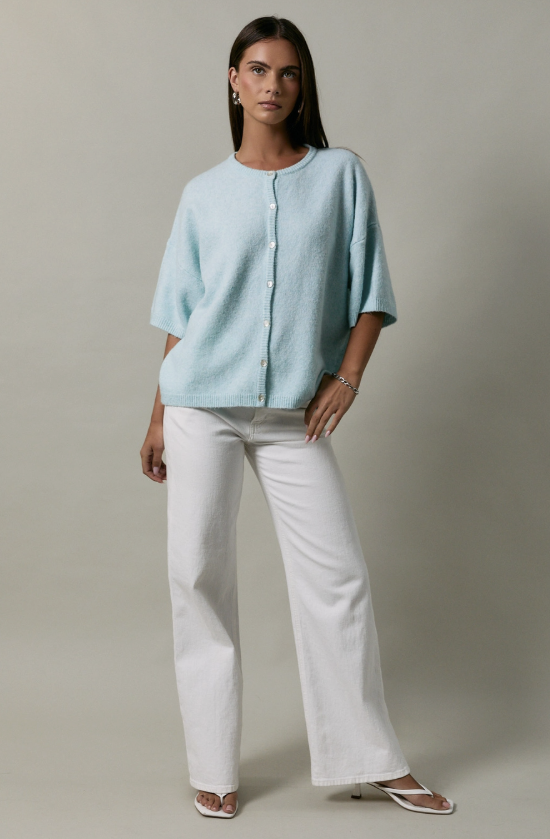 Woman wearing a light blue top and white pants against a neutral background