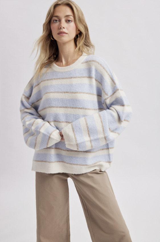 Woman wearing light blue and white stripe sweater with beige pants on plain background