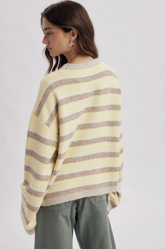 A woman wearing a cream and taupe striped fuzzy knit sweater, shown from a side-back angle against a light gray studio background.