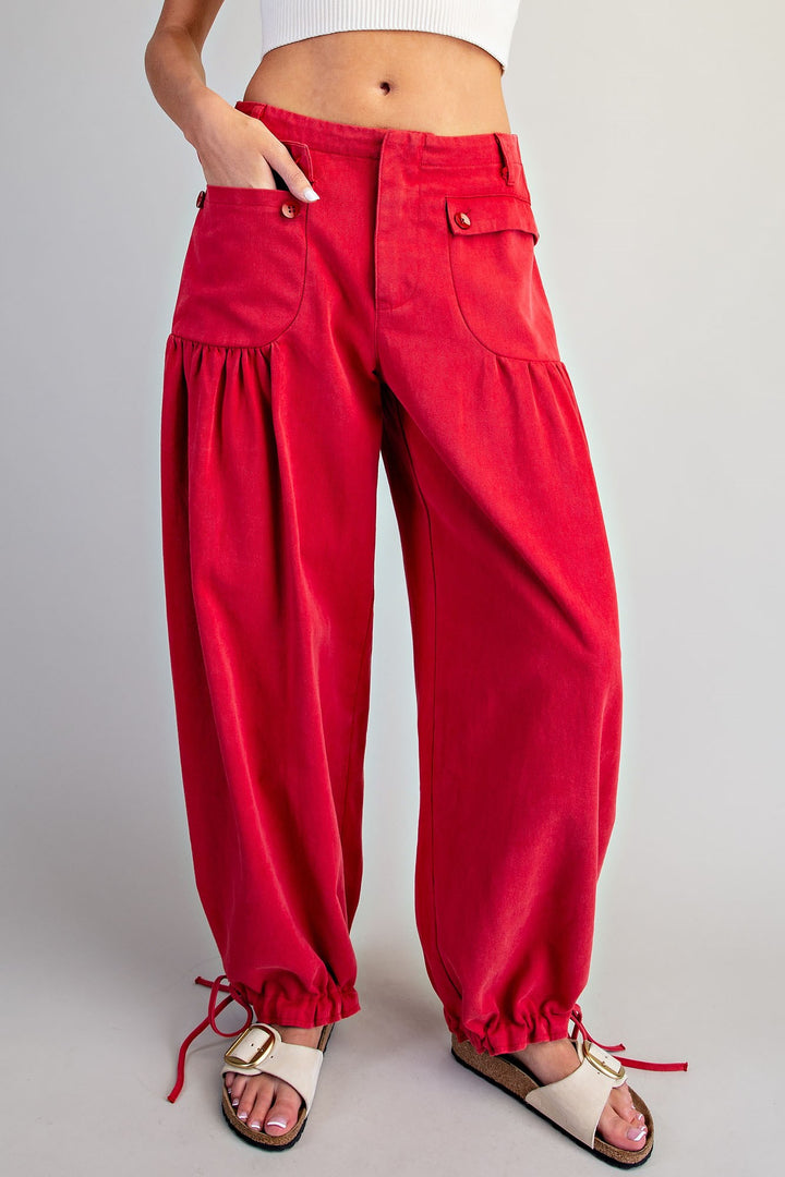 A person wearing bright red wide-leg harem-style pants with gathered legs, front flap pockets, and drawstring ankle ties, paired with white slide sandals against a light gray studio background.
