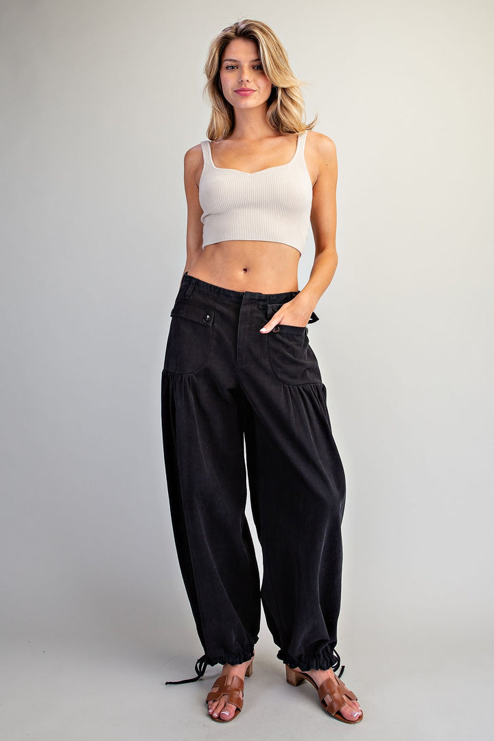 A woman modeling black wide-leg harem pants with drawstring ankle cuffs, paired with a white ribbed crop top and brown heeled sandals, against a light gray studio background.