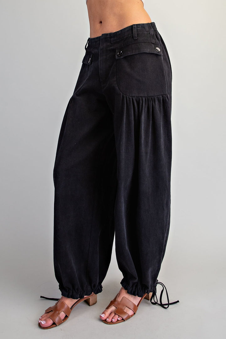 Black wide-leg harem pants with gathered balloon legs, elastic cuffs, and side tie details, shown on a model wearing brown heeled sandals against a light gray studio background.