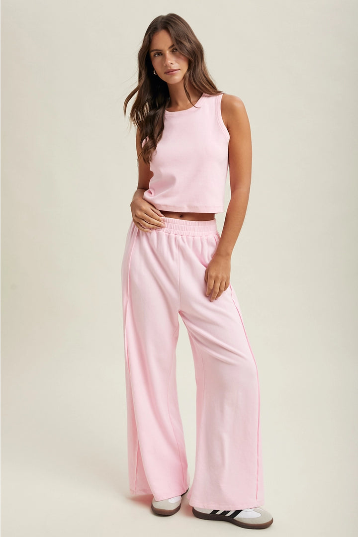 Woman wearing a pink sleeveless top and wide-leg pants on a plain background