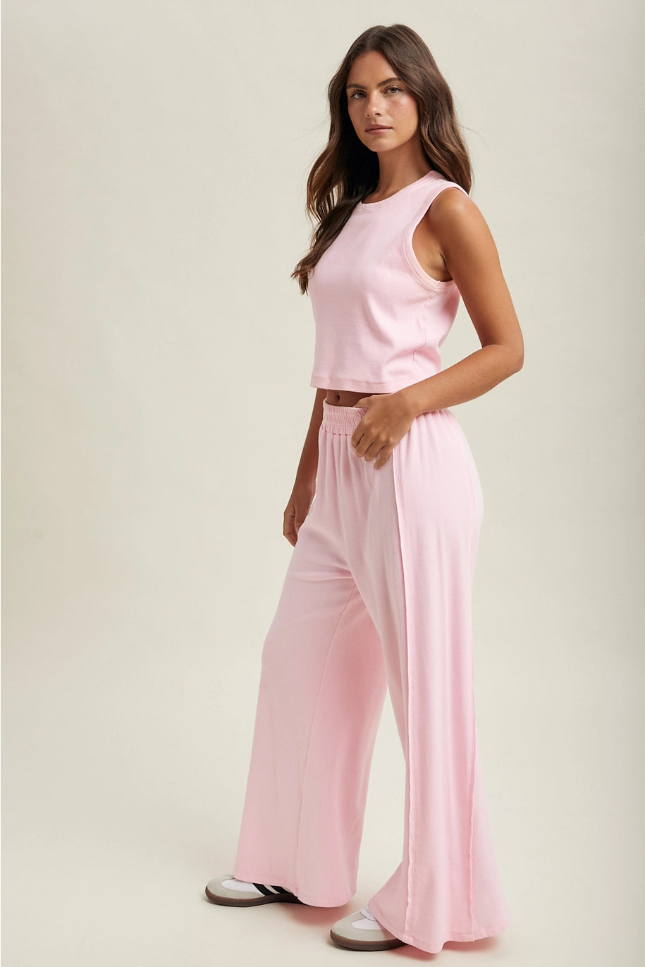 Woman wearing a pink sleeveless top and wide-leg pants on a plain background