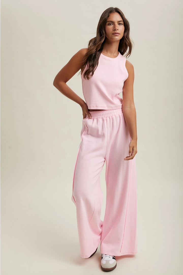 Woman wearing a pink sleeveless top and wide-leg pants on a plain background