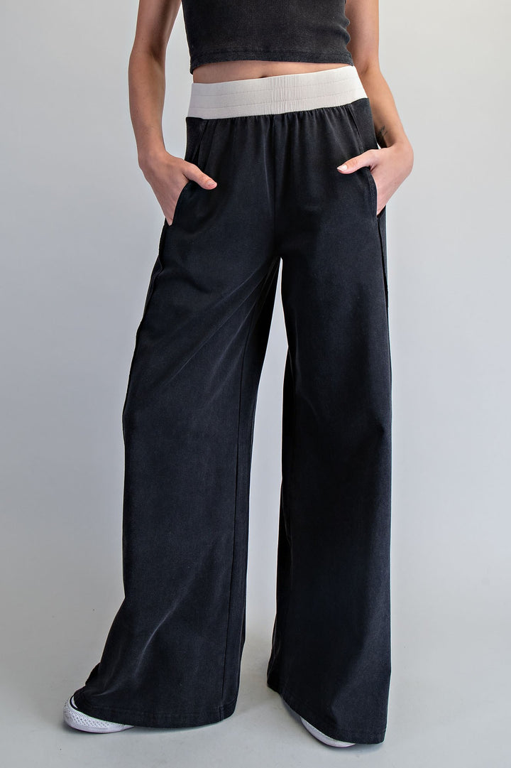 Person wearing black wide-leg pants with a white waistband on a gray background