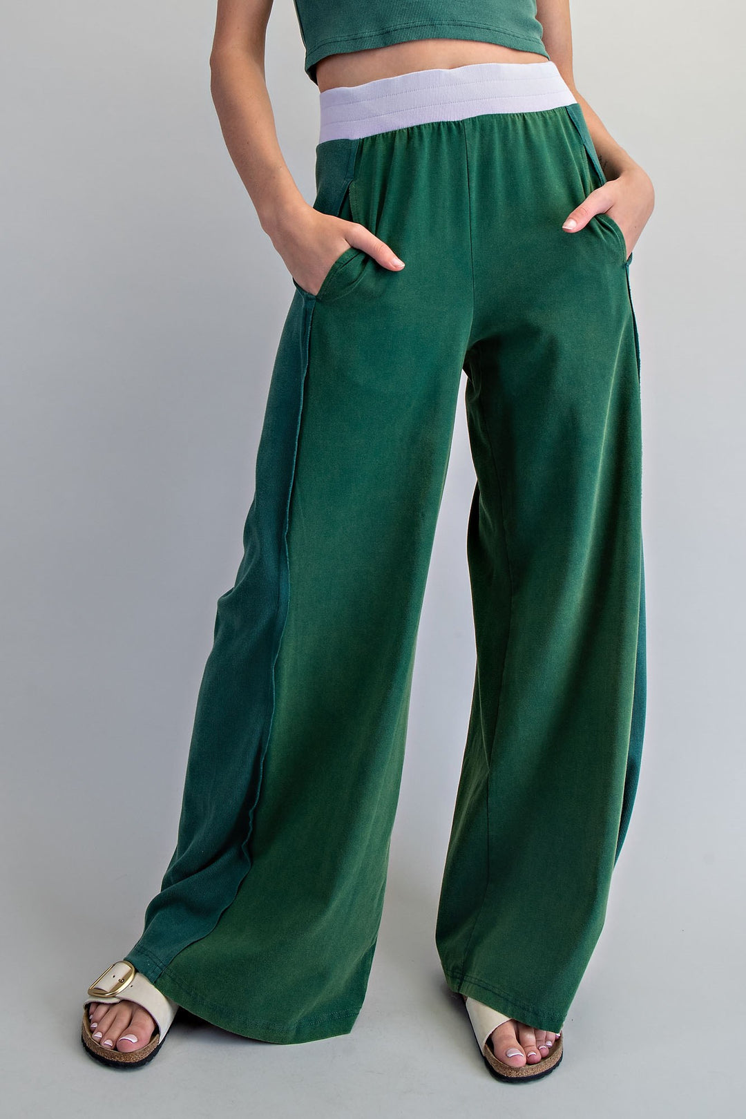Person wearing green wide-leg pants and a cropped top on a gray background
