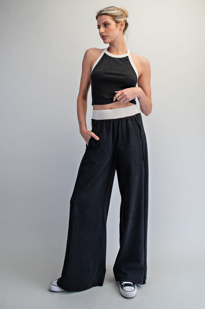 Woman wearing a black crop top and wide-leg pants on a plain background