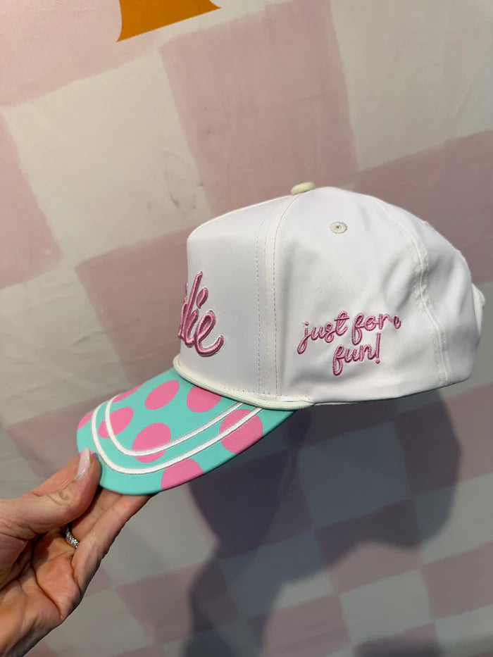 White cap with pink text and watermelon design held by a hand against a patterned background