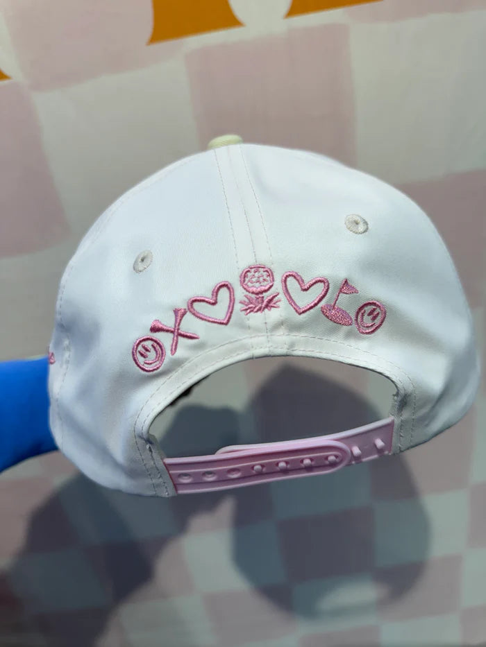 White cap with pink heart designs and text on a checkered background