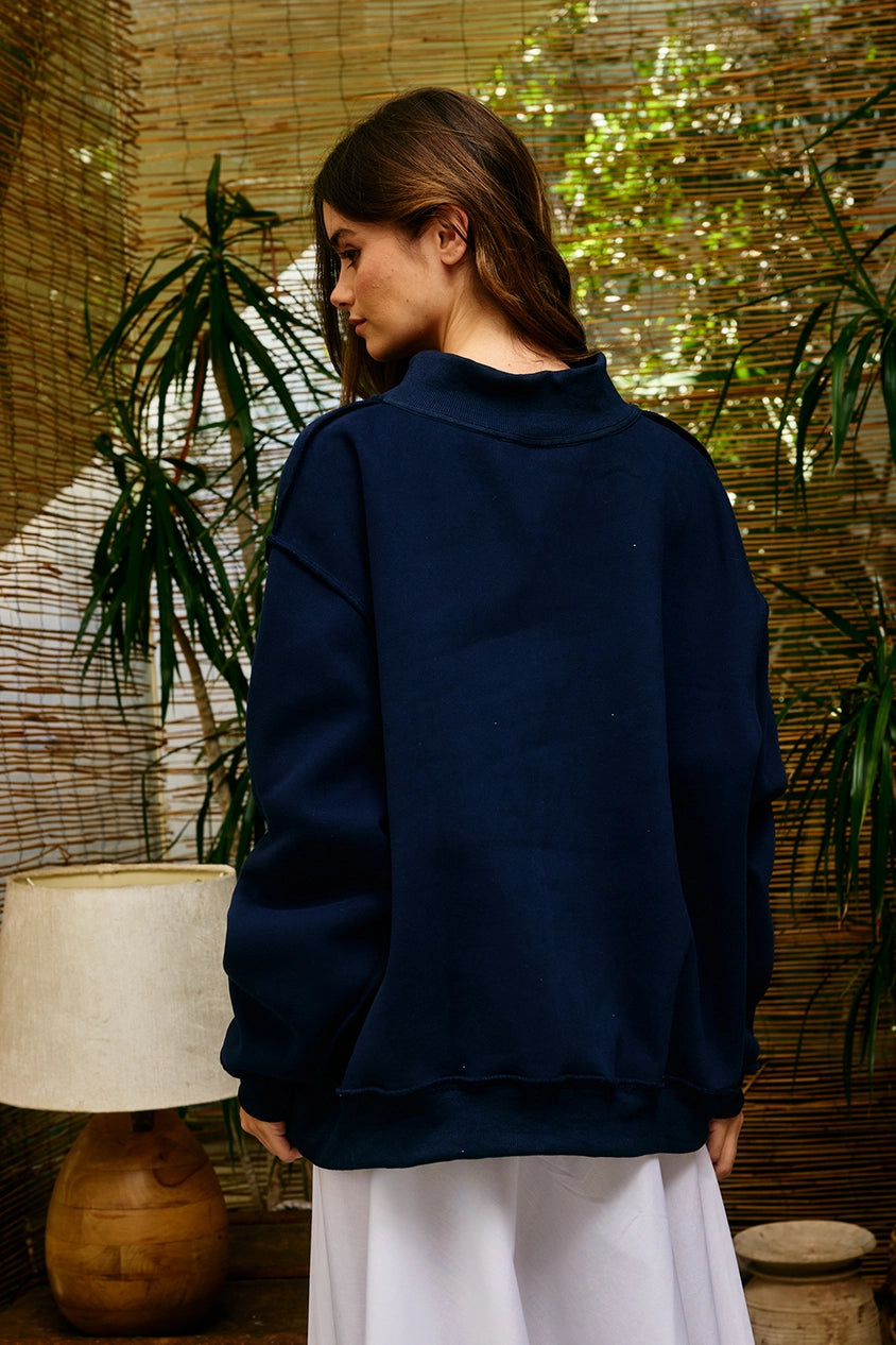 Woman wearing a navy blue sweater in a room with plants and a lamp.
