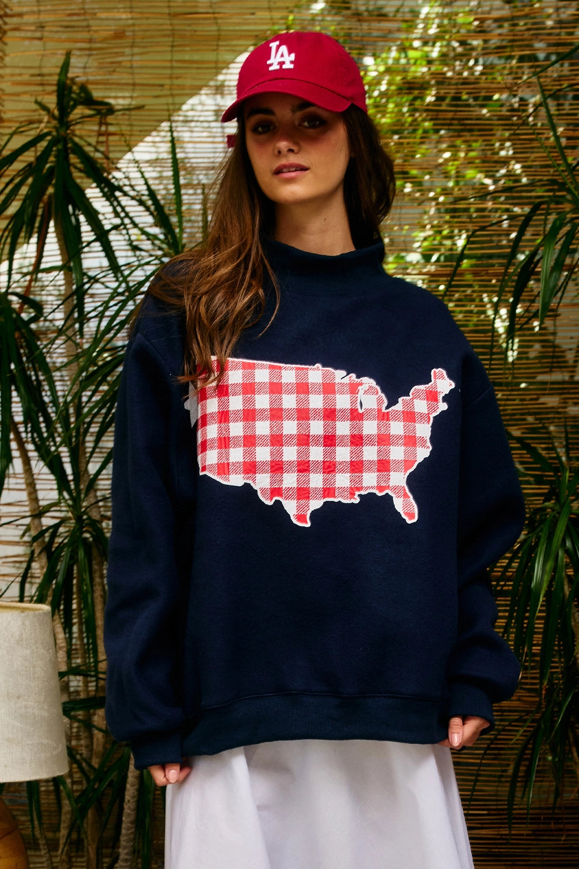 Person wearing a navy sweatshirt with a red and white USA map design, standing against a natural background.