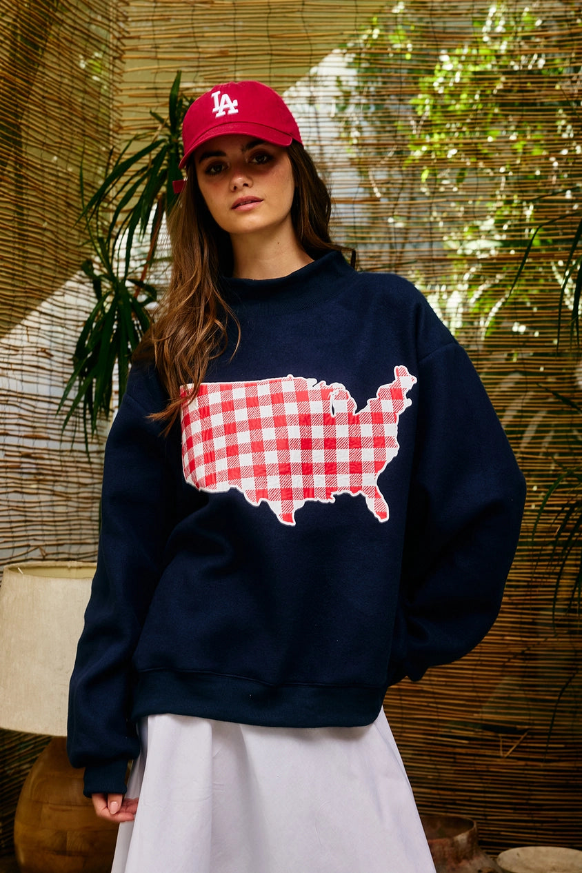 Person wearing a navy sweatshirt with a red and white map design, a red cap, and white pants against a natural background.